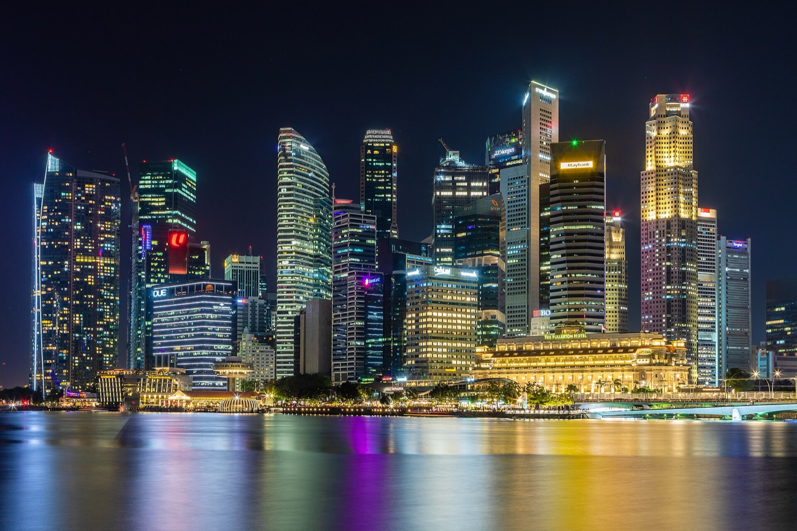 Singapore's business district across Marina Bay at night, with the Fullerton Hotel in front